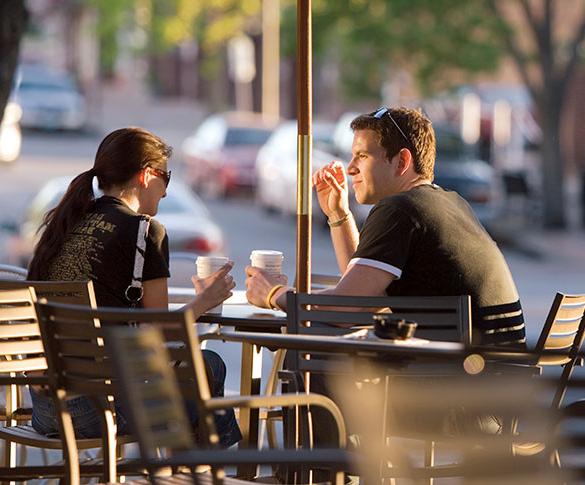 Man and woman drinking coffee at cafe table on downtown sidewalk